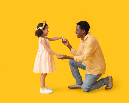 Little African-American girl and her father on yellow backgroundの写真素材