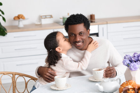 Happy little African-American girl kissing her father in the kitchenの写真素材