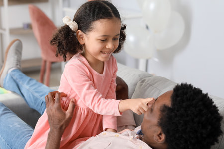 Happy African-American man and his little daughter playing at homeの写真素材