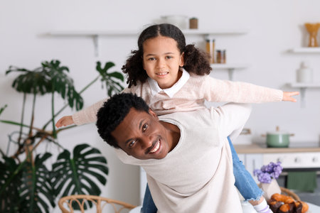 Happy African-American man and his little daughter playing in the kitchenの写真素材