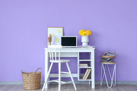 Workplace with modern laptop and vase with flowers near color wall in room interiorの写真素材