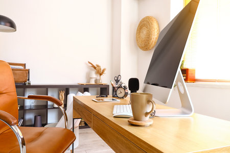 Modern computer, microphone and cup on table in light room, closeupの写真素材