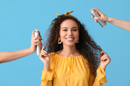 Beautiful young African-American woman and hands with hair spray on blue backgroundの写真素材