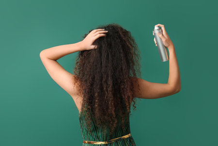 Pretty young African-American woman with hair spray on green background, back viewの写真素材