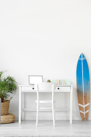 Workplace with modern laptop and surfboard near white wall in roomの写真素材