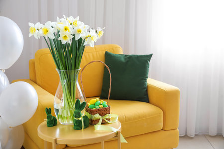 Vase with flowers, Easter bunnies and eggs on table near armchair in roomの写真素材