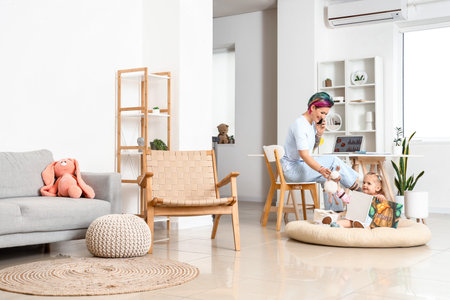 Little girl with book and her working mother at homeの写真素材