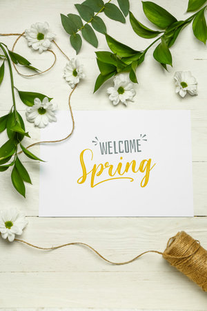 Card with text WELCOME SPRING, flowers, plant branches and rope on light wooden backgroundの写真素材