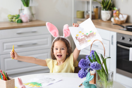 Happy little girl with bunny ears and Easter greeting card in kitchen at homeの写真素材