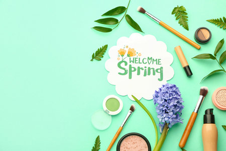 Card with text WELCOME SPRING, decorative cosmetics, makeup brushes and plant leaves on color...