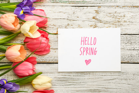 Card with text HELLO SPRING and beautiful flowers on light wooden background