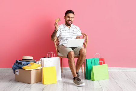 Handsome man with laptop, credit card and shopping bags on pink backgroundの写真素材