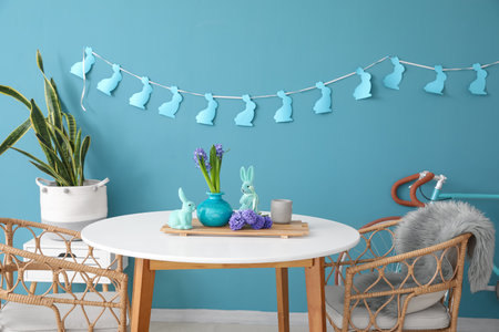 Vase with hyacinth flowers, Easter rabbits on table and chairs near color wall