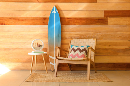 Table with planter, surfboard and armchair near wooden wallの写真素材