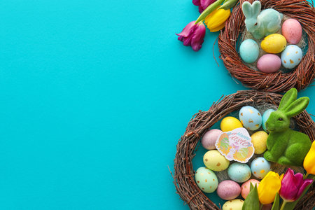 Nests with beautiful Easter eggs, bunnies and tulip flowers on color background