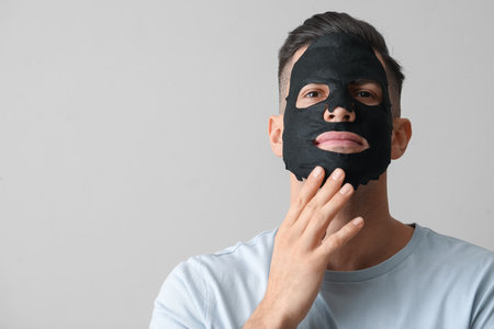 Handsome man with black facial mask on gray backgroundの写真素材