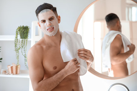 Handsome man with facial mask and towel in bathroomの写真素材