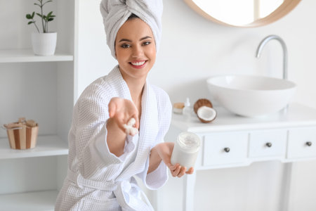 Young woman with jar of coconut oil in bathroomの写真素材