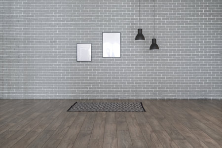Carpet, lamps and blank frames hanging on gray brick wall in big room