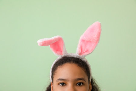 Cute African-American girl with bunny ears on color background. easter celebrationの写真素材