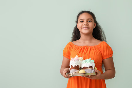 Cute African-American girl with Easter cakes on color background