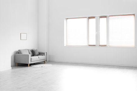 Gray sofa and frame hanging on light wall in empty roomの写真素材