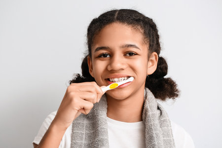 African-American teenage girl brushing teeth on light background