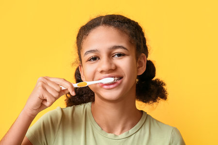 African-American teenage girl brushing teeth on yellow background