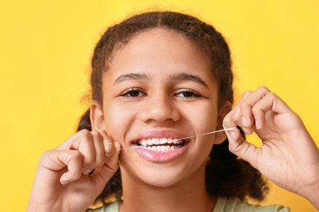 African-American teenage girl flossing teeth on yellow background, closeup