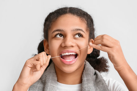 African-American teenage girl flossing teeth on light backgroundの写真素材