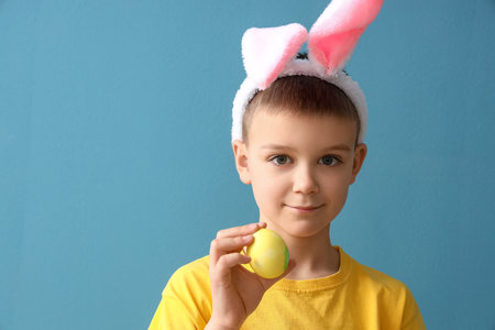 Cute little boy with bunny ears and Easter egg on blue background