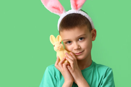 Cute little boy with bunny ears and toy rabbit on green background. easter celebration