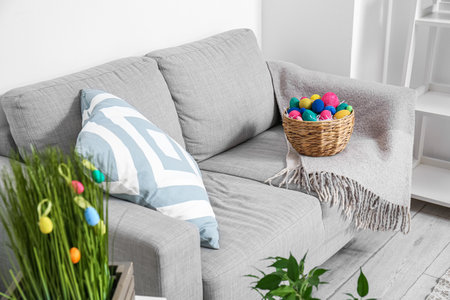 Wicker basket with Easter eggs on sofa near light wallの写真素材
