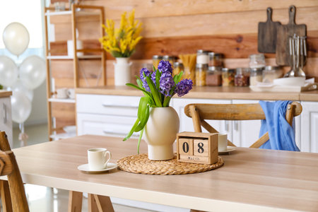 Cube calendar with date 8 MARCH, flowers and cup of coffee on dining table in kitchen. International Women's Day celebrationの写真素材