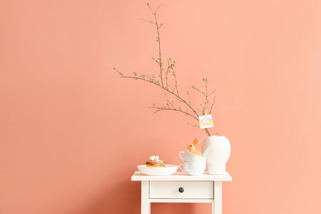 Delicious bun, cups, tree branches and greeting card with text HAPPY EASTER in vase on table near...