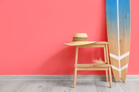 Wooden surfboard and table with hat near pink wall
