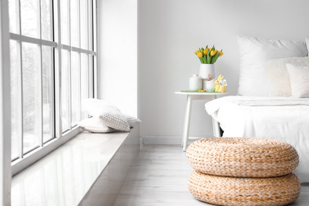 Vase with tulips, cups and Easter rabbits on table near light wall in bedroom interiorの写真素材