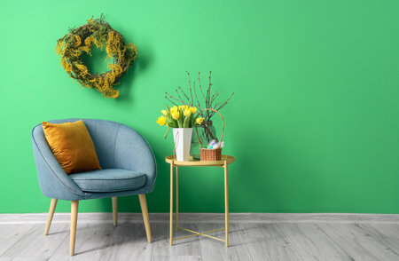 Comfortable armchair, table with tulips and basket of Easter eggs near color wallの写真素材