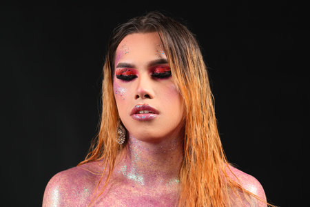 Fashionable young transgender woman with glitters on body against dark background