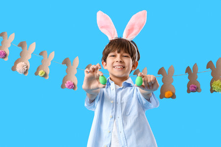 Adorable little boy with bunny ears and Easter eggs on blue backgroundの写真素材