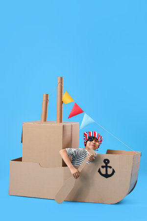 Cute little boy playing with cardboard ship on blue backgroundの写真素材