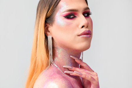 Fashionable young transgender woman with glitters on body against light background