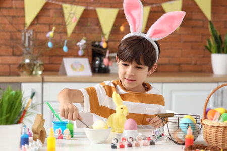 Cute little boy painting Easter eggs in the kitchen at home