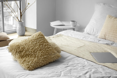 Soft pillows and laptop on bed in light room