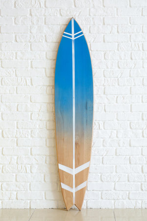 Modern surfboard near white brick wall in roomの写真素材