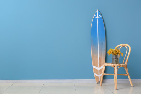 Vase with mimosa flowers on chair and surfboard near color wall in roomの写真素材