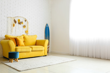 Comfortable sofa, pouf and surfboard near white brick wall in light room interiorの写真素材