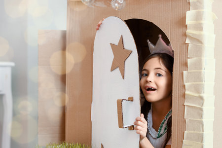 Funny little girl playing with cardboard house at homeの写真素材