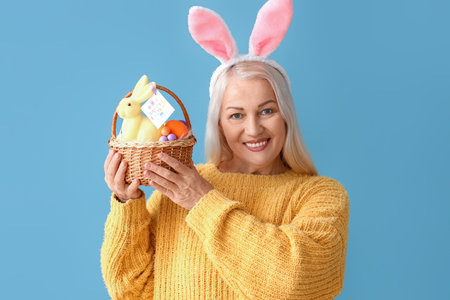 Mature woman with bunny ears and Easter basket on blue backgroundの写真素材
