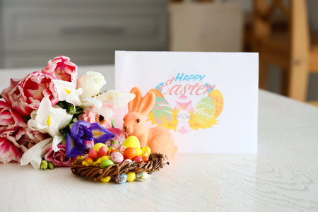Nest with Easter eggs, rabbit, beautiful flowers and greeting card with text HAPPY EASTER on dining tableの写真素材